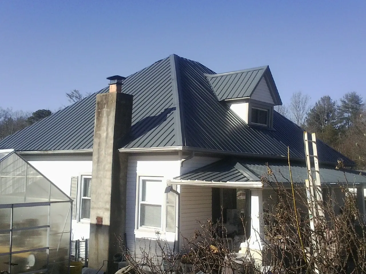 Dark blue standing seam metal roof on a white farmhouse with dormer — Slate & Tile Roof Repair by Roofing Brothers in Bluemont