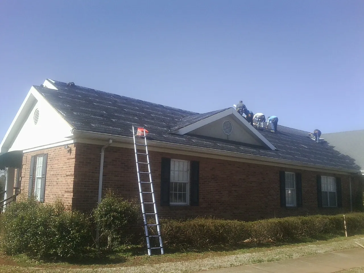 Crew tearing shingles off a brick ranch roof with a ladder set — Emergency Roof Repair work by our crew in Bluemont