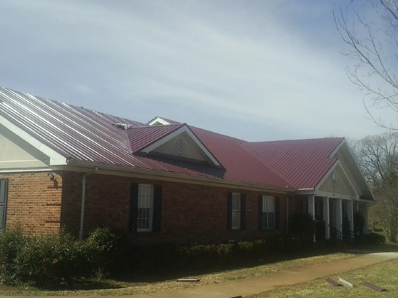 Red metal roof with gabled entries on a long brick building, from a Hail Damage Roof Repair job in Bluemont