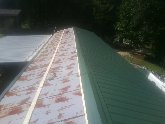 Old rusted panels beside newly installed green metal roofing — Wind Damage Roof Repair by Roofing Brothers in Bluemont