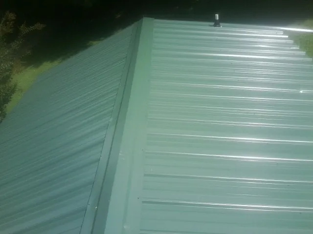 New green metal panels meeting at the ridge of a roof — Flat Roof Repair work by our crew in Bluemont