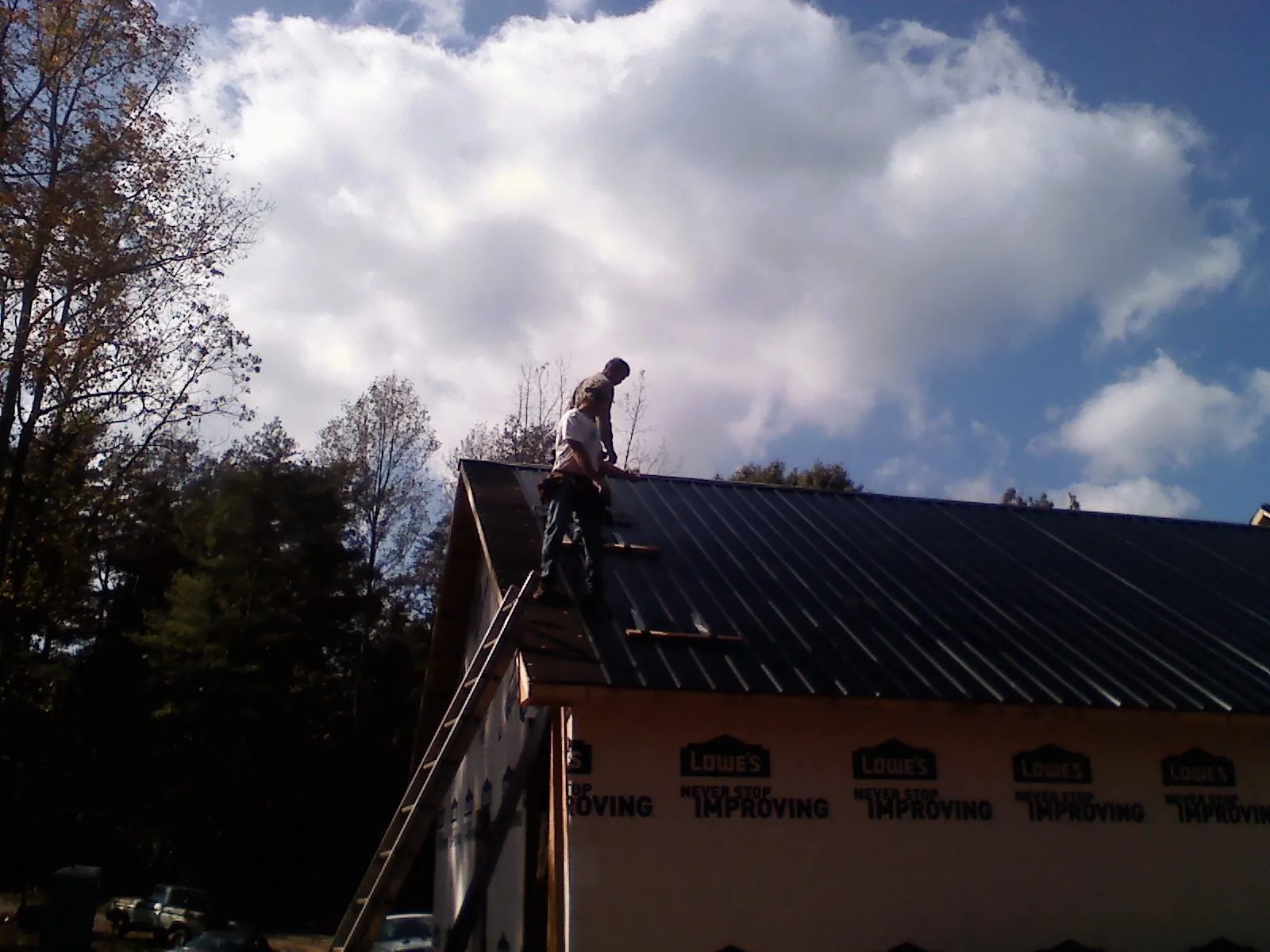 Roofer fastening dark metal panels high against a cloudy sky, from a Roof Inspection job in Bluemont
