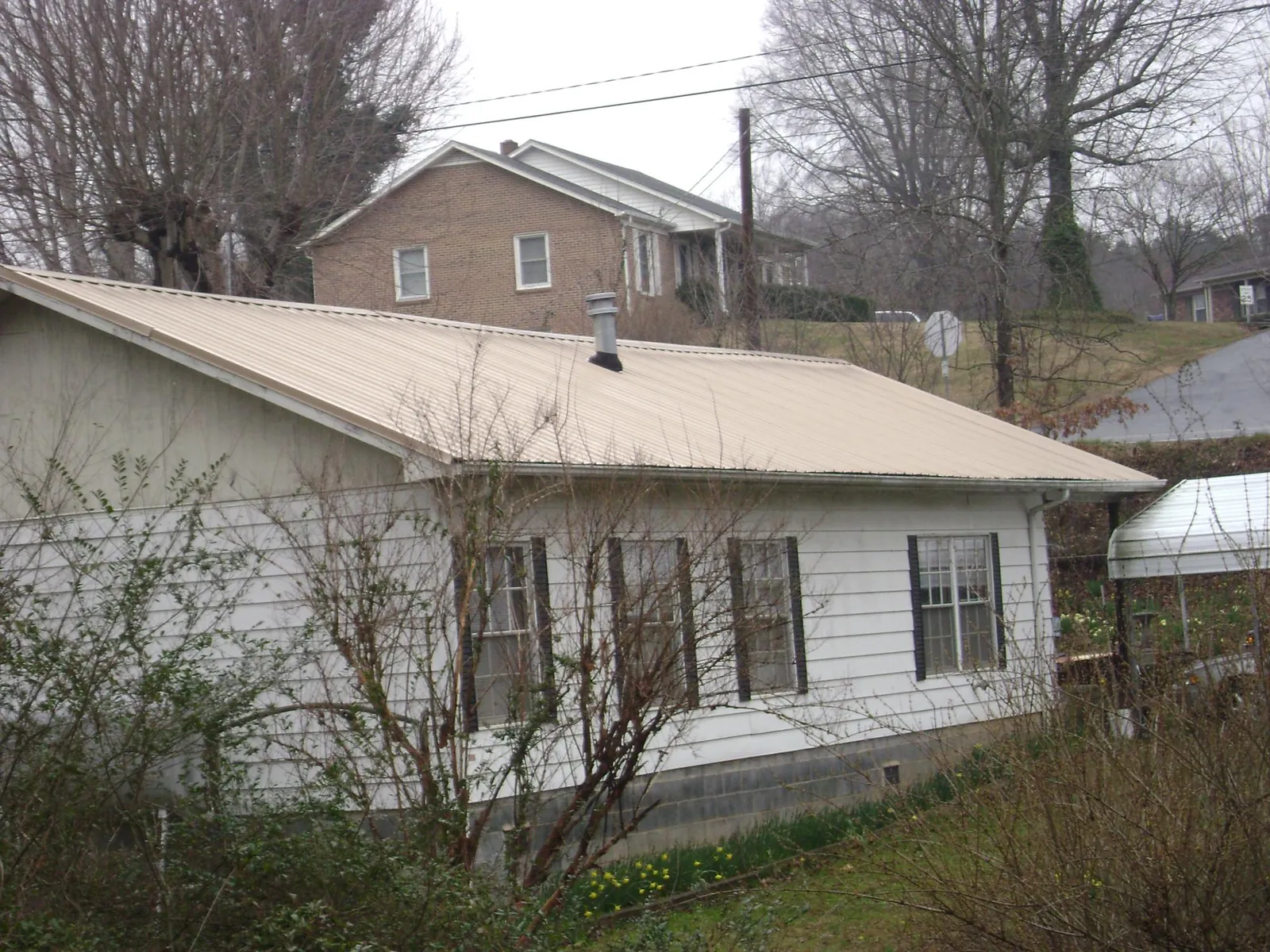 Tan metal roof on a white sided house set into a hillside — Commercial Roofing by Roofing Brothers in Bluemont